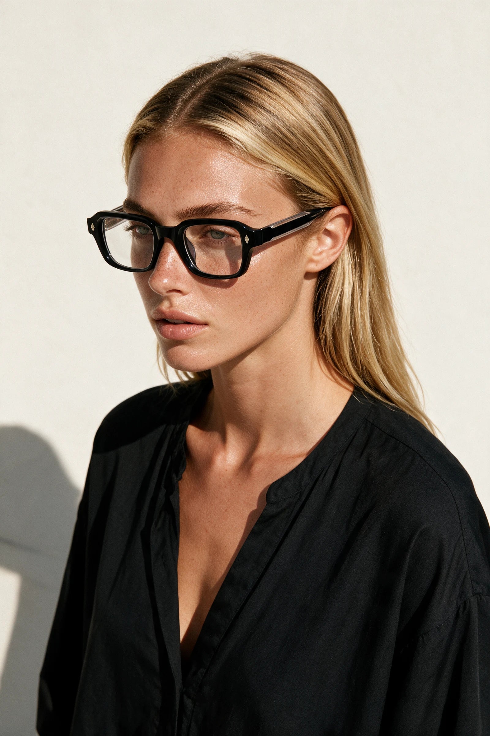 Woman wearing VELA Clear glasses, shot from a high angle against a warm bone backdrop