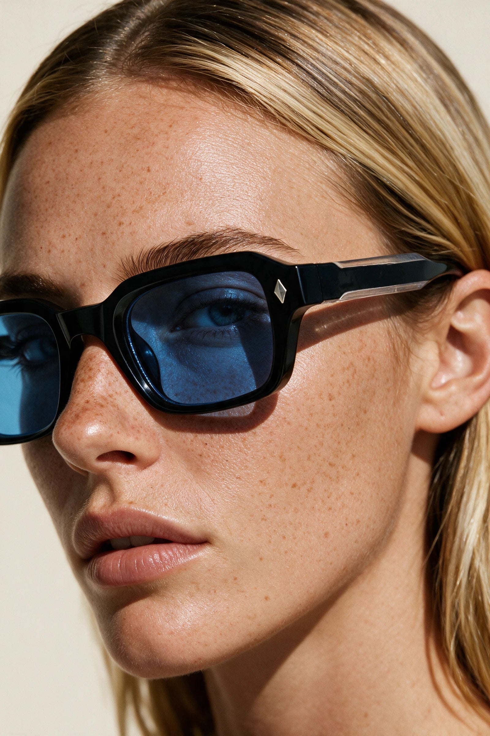 Close-up of VELA Cobalt sunglasses showing the keyhole bridge, silver diamond stud and clear band along the temple