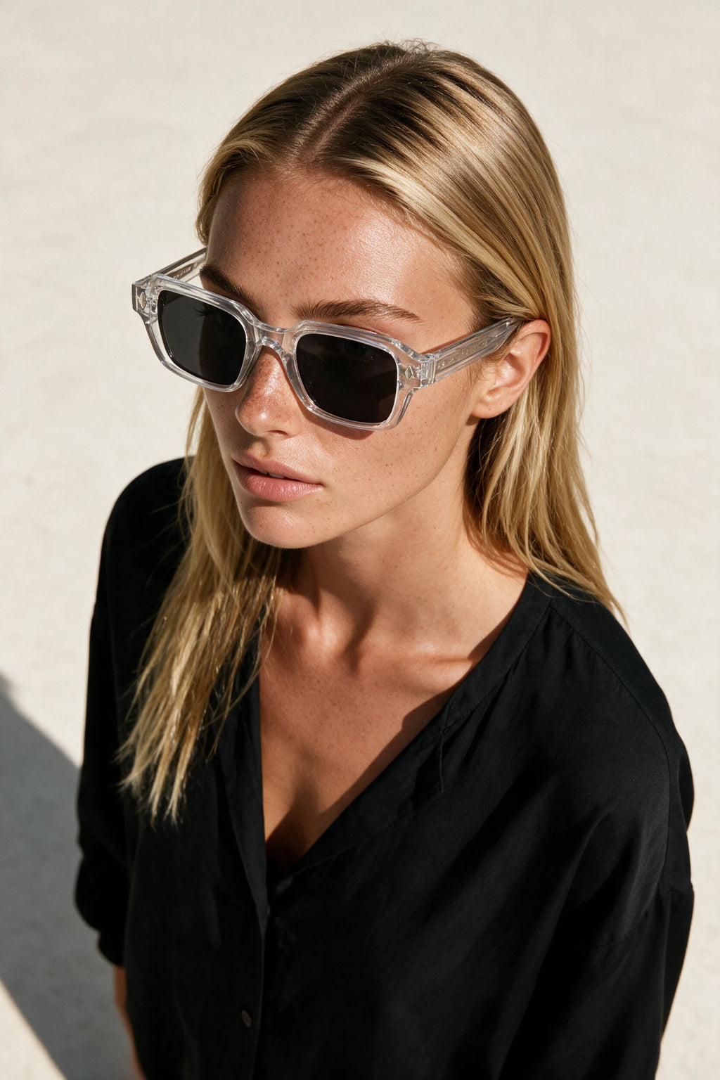 Woman wearing VELA Crystal sunglasses, shot from a high angle against a warm bone backdrop