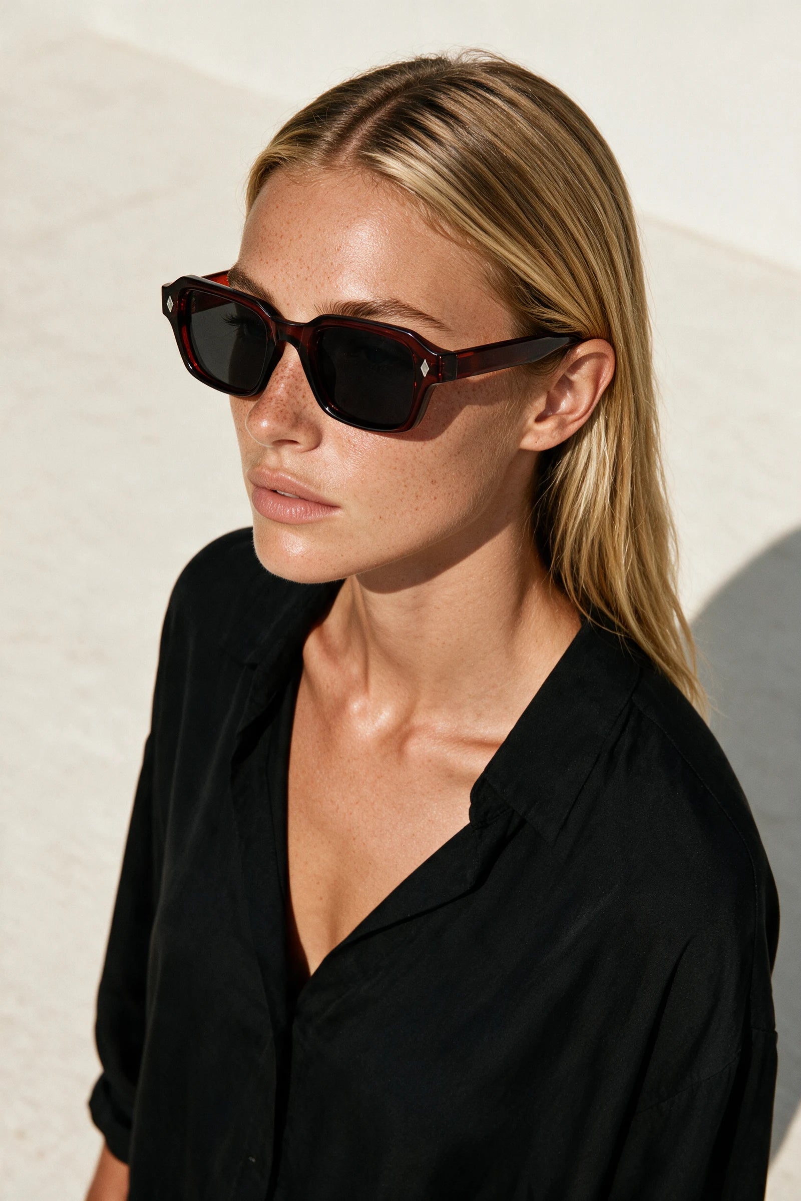 Woman wearing VELA Oxblood sunglasses, shot from a high angle against a warm bone backdrop
