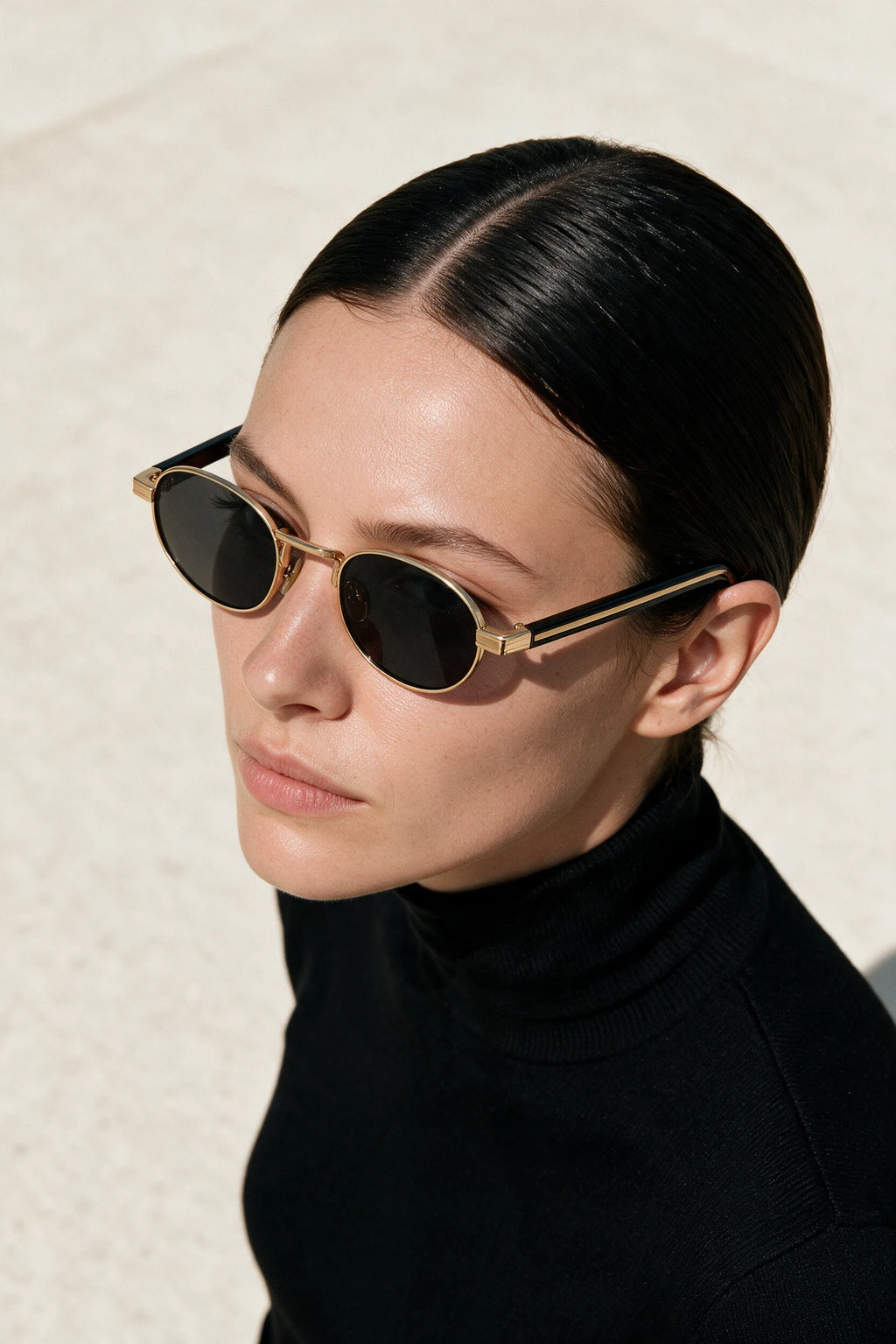 Woman wearing MARA oval sunglasses in black and gold with smoke lenses