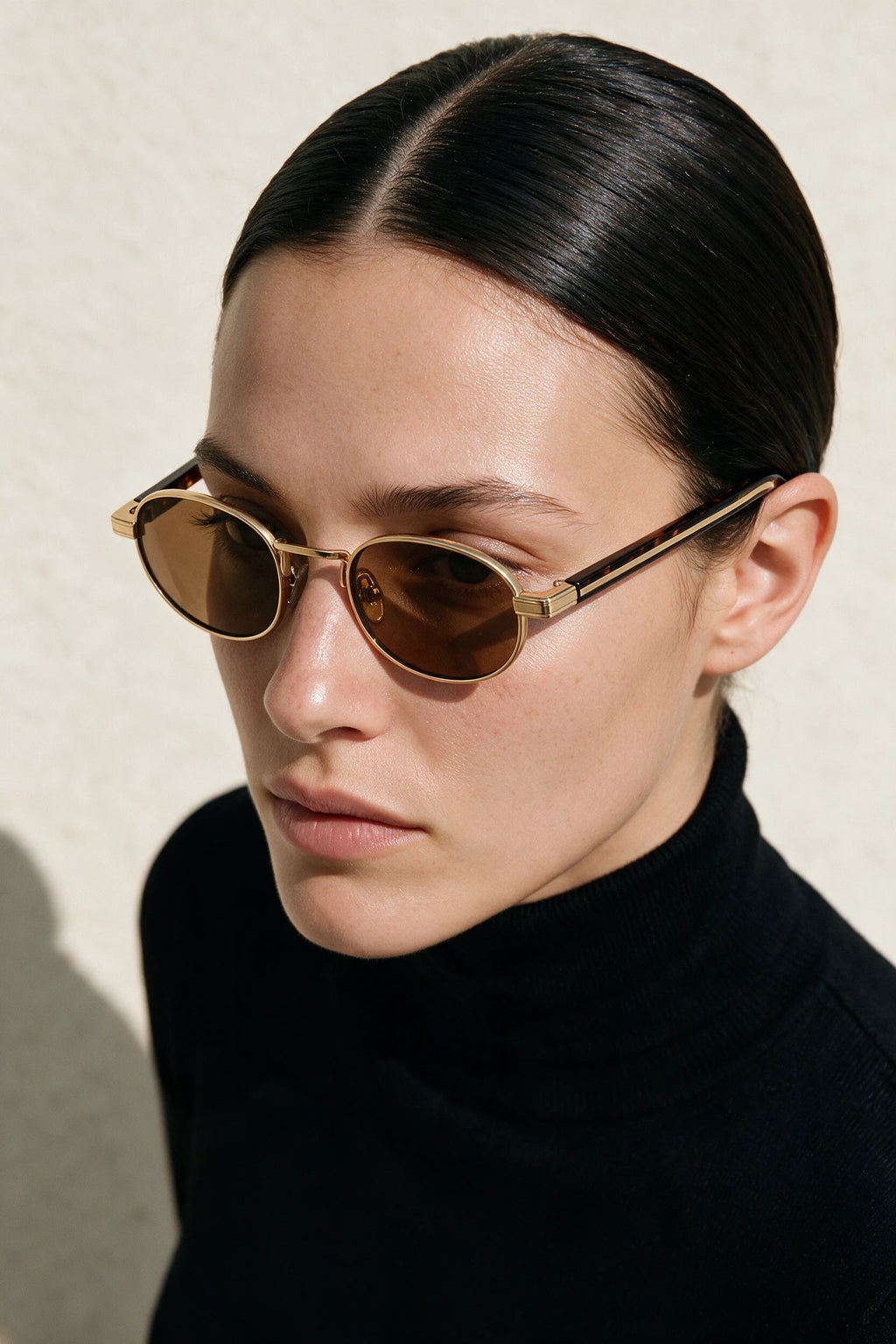 Woman wearing MARA oval sunglasses in gold with tortoiseshell temples and tea lenses