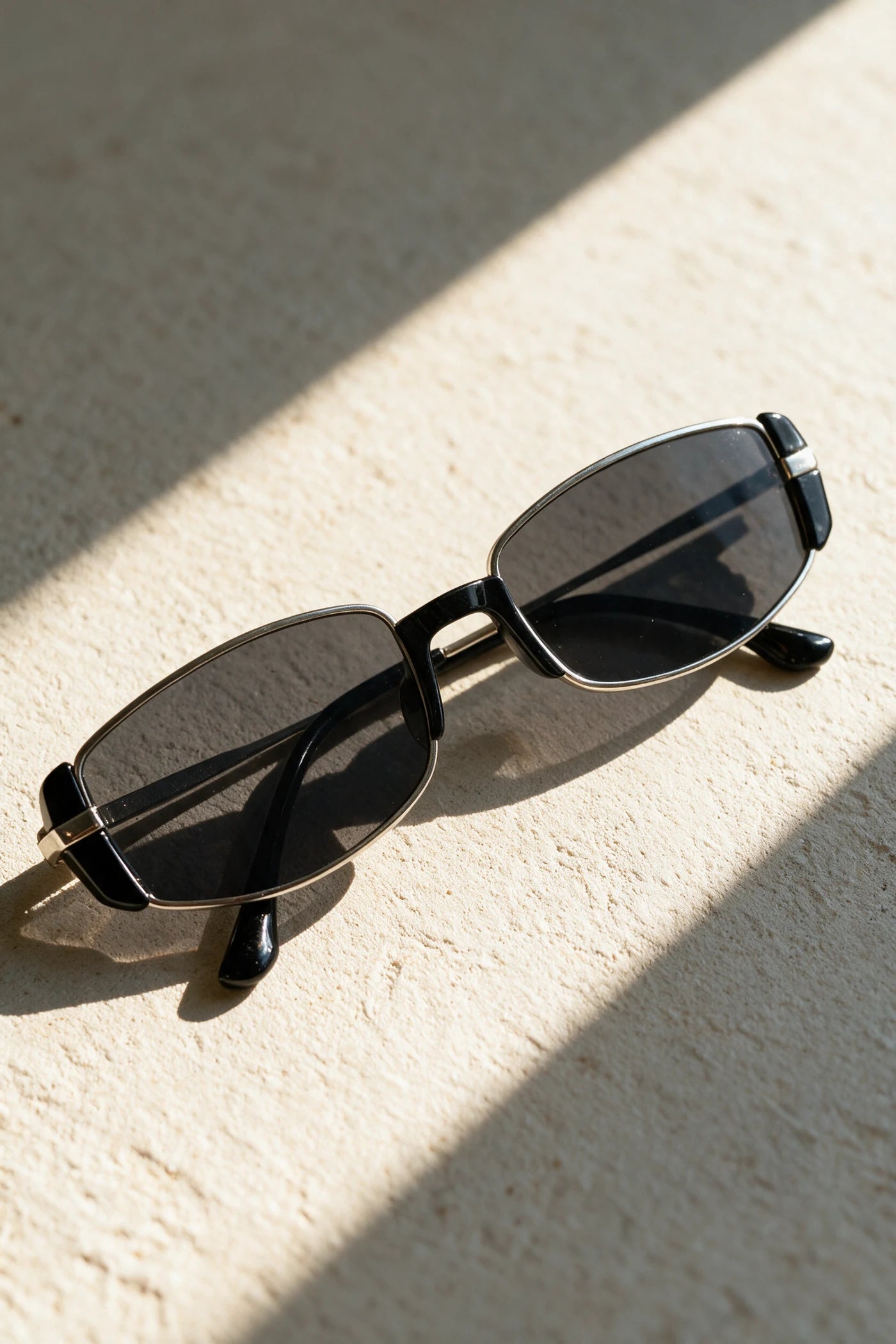 NEVA sunglasses in silver folded on a warm bone plaster surface in raking sunlight