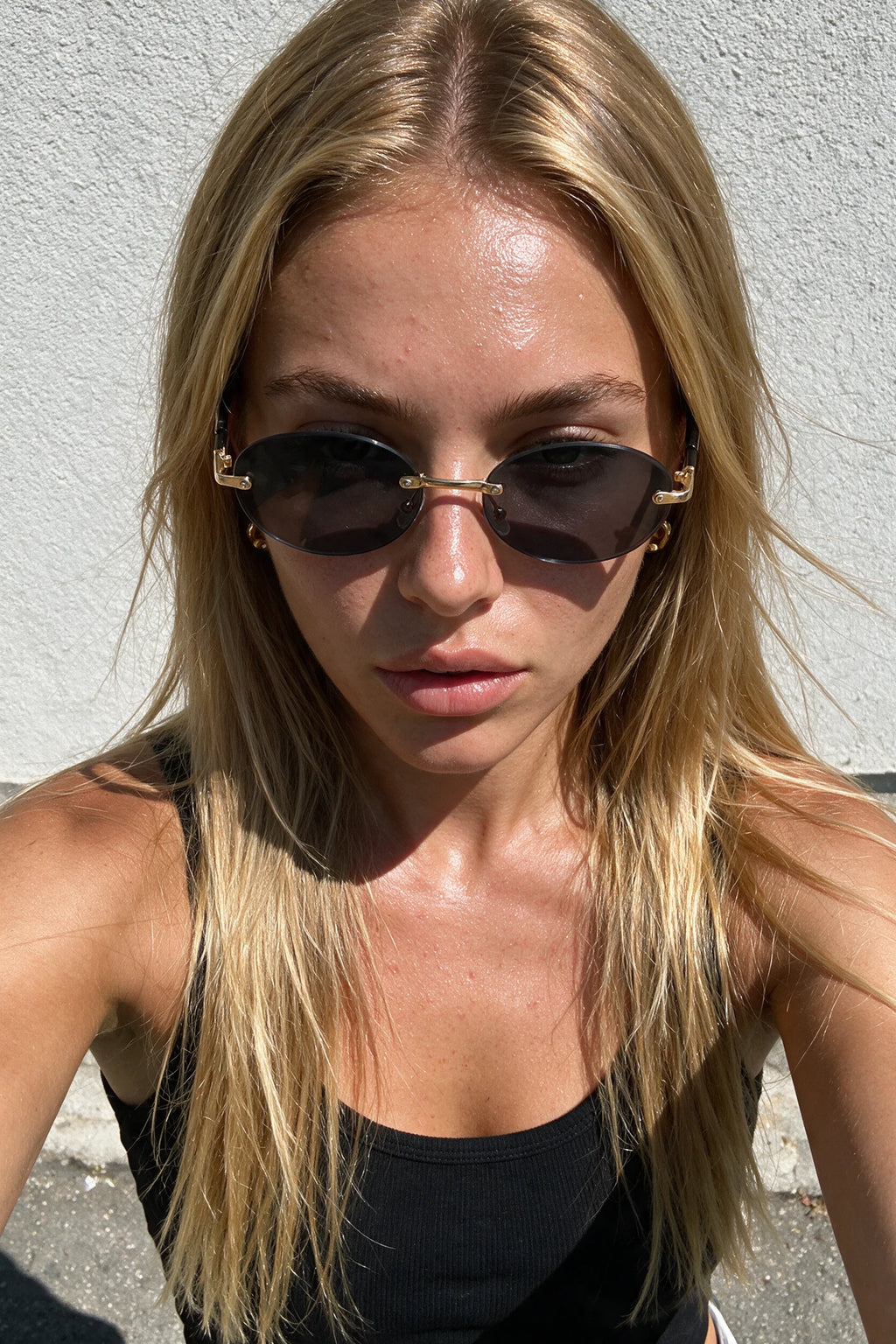 SERA rimless oval sunglasses in smoke black worn outdoors in bright sunlight