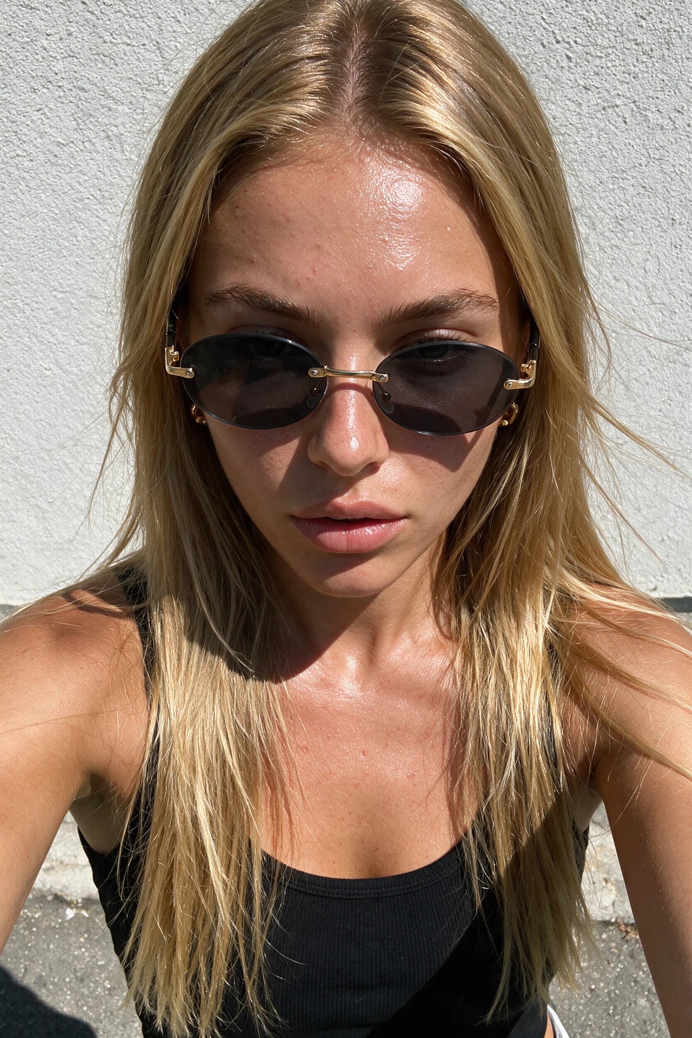 SERA rimless oval sunglasses in smoke black worn outdoors in bright sunlight